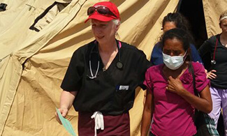 Kathy Bogacz, M.D., leads elderly woman to emergency care during LUCOM medical outreach, 2016.